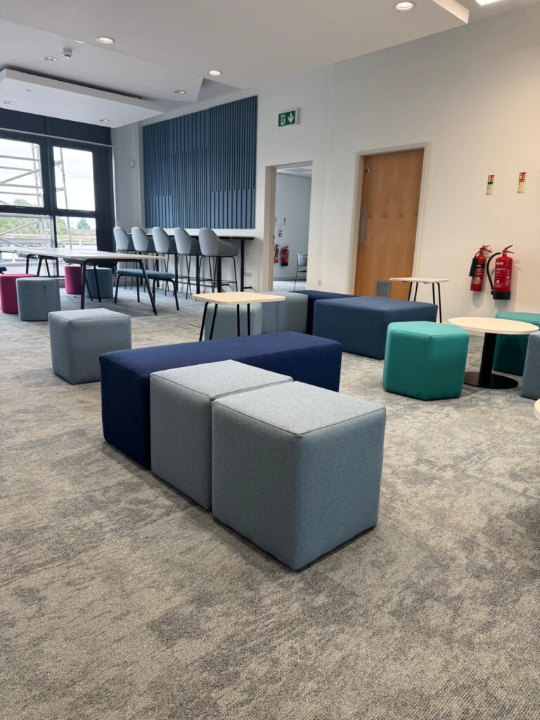 Grey upholstered cubes beside a long navy bench, with other seating and high stools beyond.