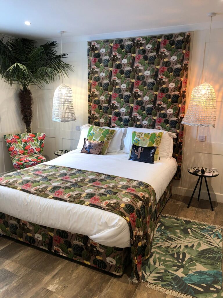 Bedroom with a tall cactus-print headboard, matching bed base and runner, beside a floral chair.