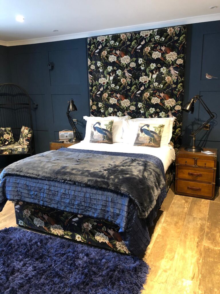 Bedroom with a tall bird-and-flower patterned headboard and matching bed base against blue panelling.