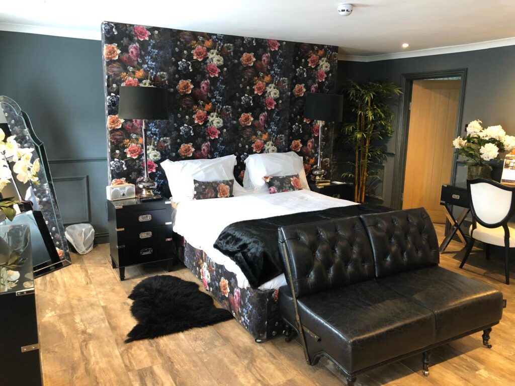 Bedroom with a tall dark floral headboard, matching upholstered bed base and a black buttoned sofa.