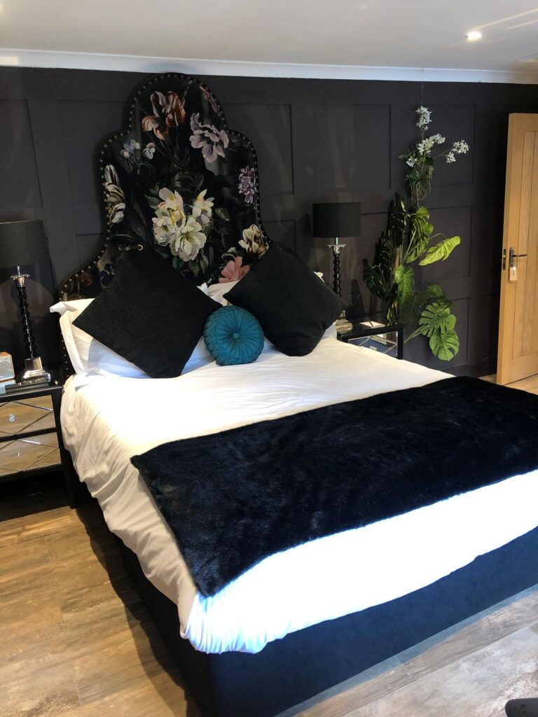 Dark bedroom with a tall curved floral headboard edged with decorative studs.