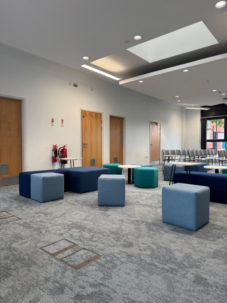 Blue, teal and grey seating across a light interior, with rows of grey chairs at the far end.