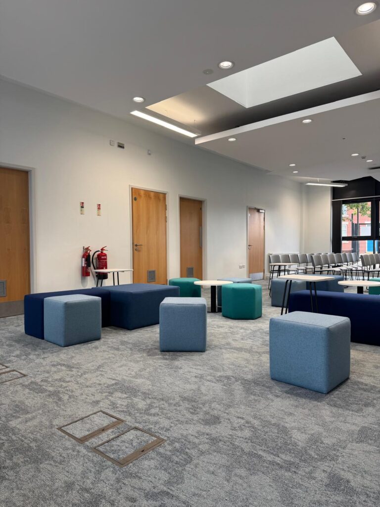 Wide view of grey cube stools, navy rectangular benches and teal seats under a white ceiling.