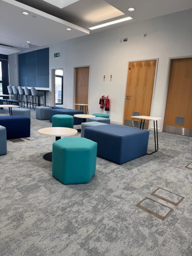 Teal hexagonal stool and a large blue upholstered block beside small white tables.