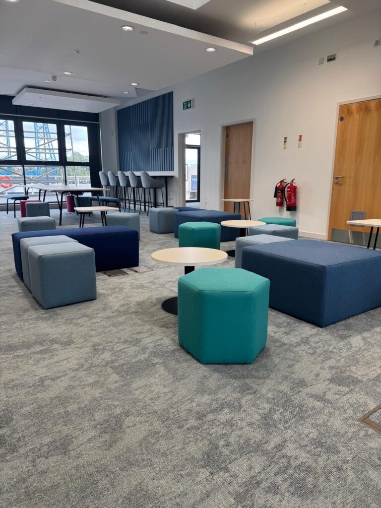 Teal stool, blue benches and grey cubes arranged around white tables beneath a blue feature wall.
