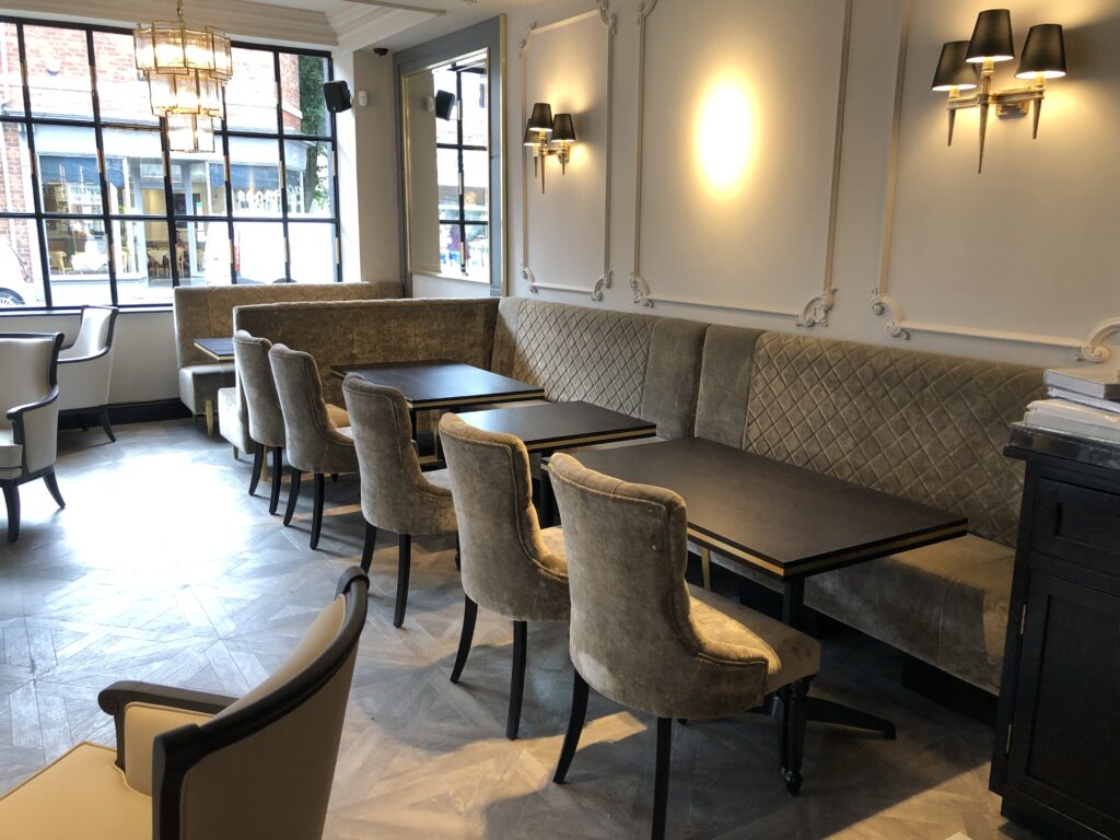 Long quilted banquette and upholstered chairs alongside tables in the lighter window-facing interior.