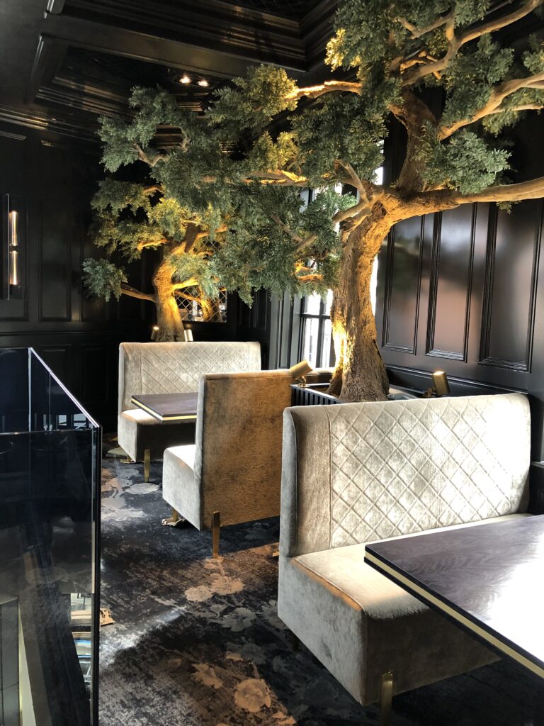 Upholstered booths with diamond-quilted backs beside large decorative trees and dark wall panelling.