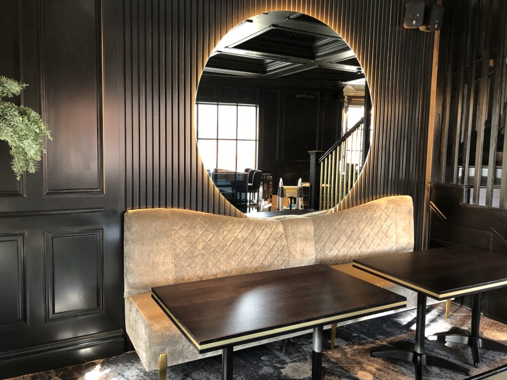 Diamond-quilted upholstered banquette beneath a round illuminated mirror at Signature North East, Whitley Bay.