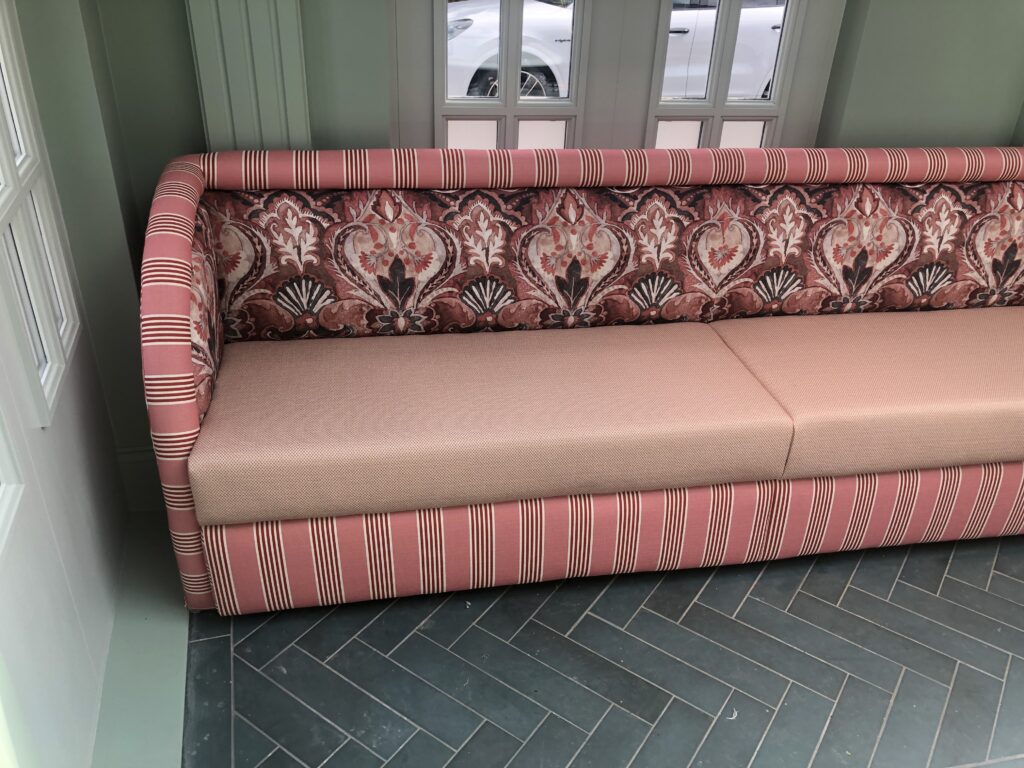 Corner detail where pink patterned backs, striped rolls and plain seats meet.