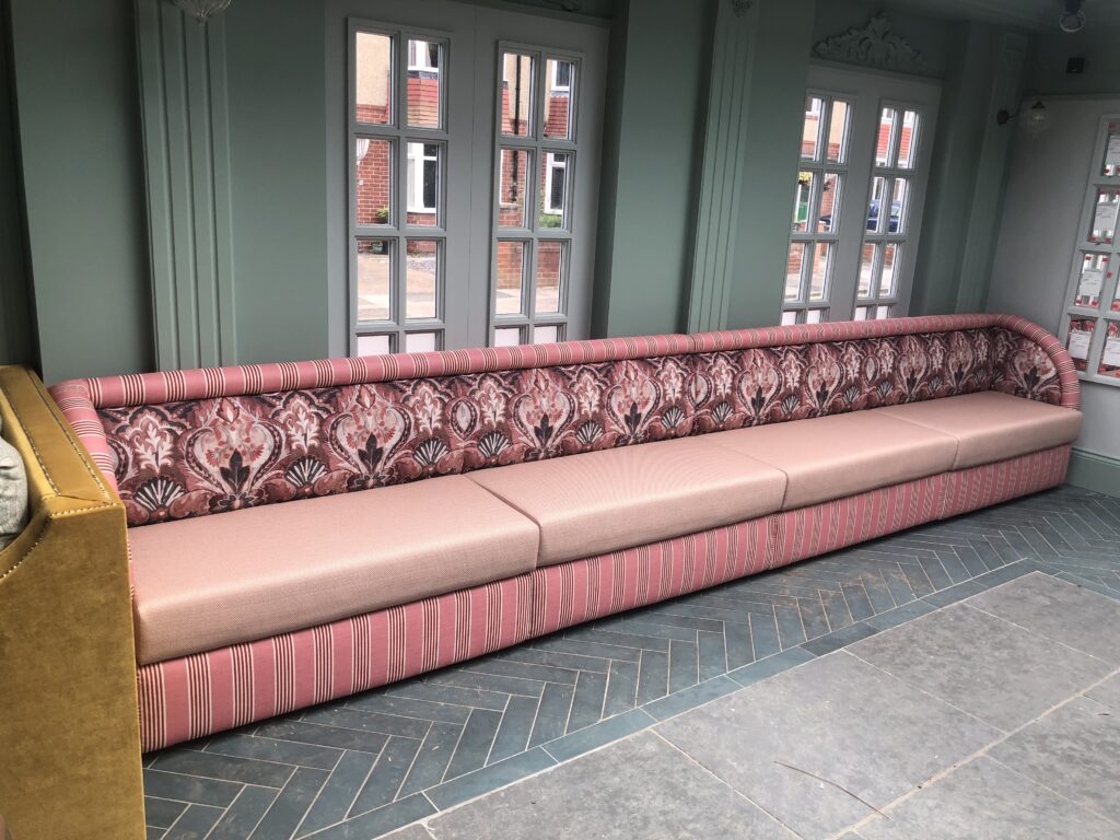 Full-length pink banquette with a patterned back, striped top roll and pale pink seats.