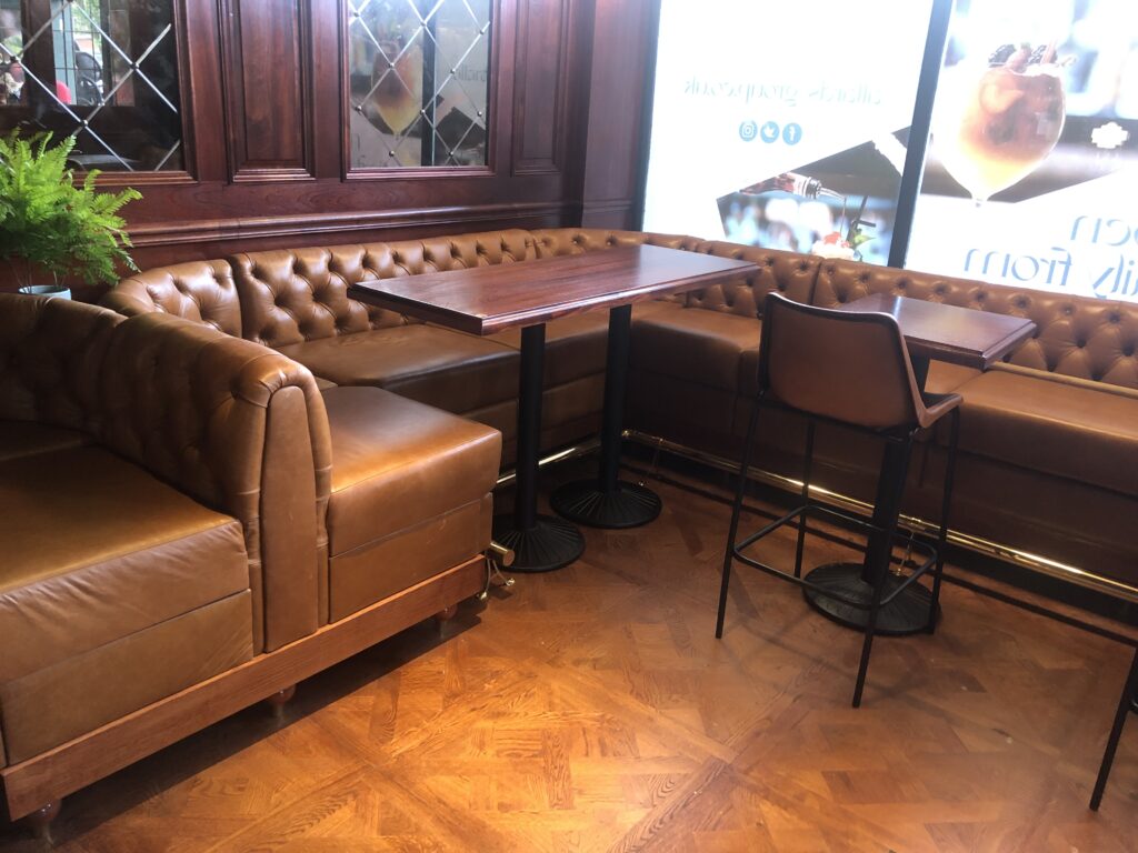 Tan buttoned corner seating around timber tables with a metal footrail below.