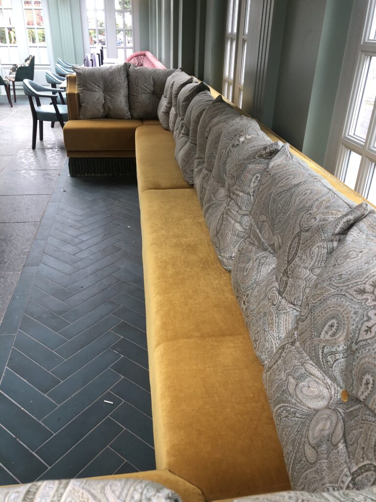 Long mustard banquette with grey paisley-patterned cushions beneath green wall panelling.