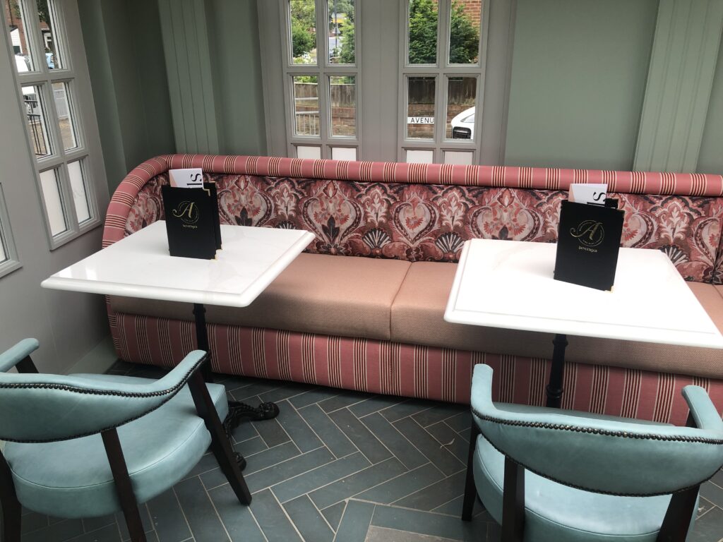 Pink banquette wrapping around a corner behind white tables and blue dining chairs.