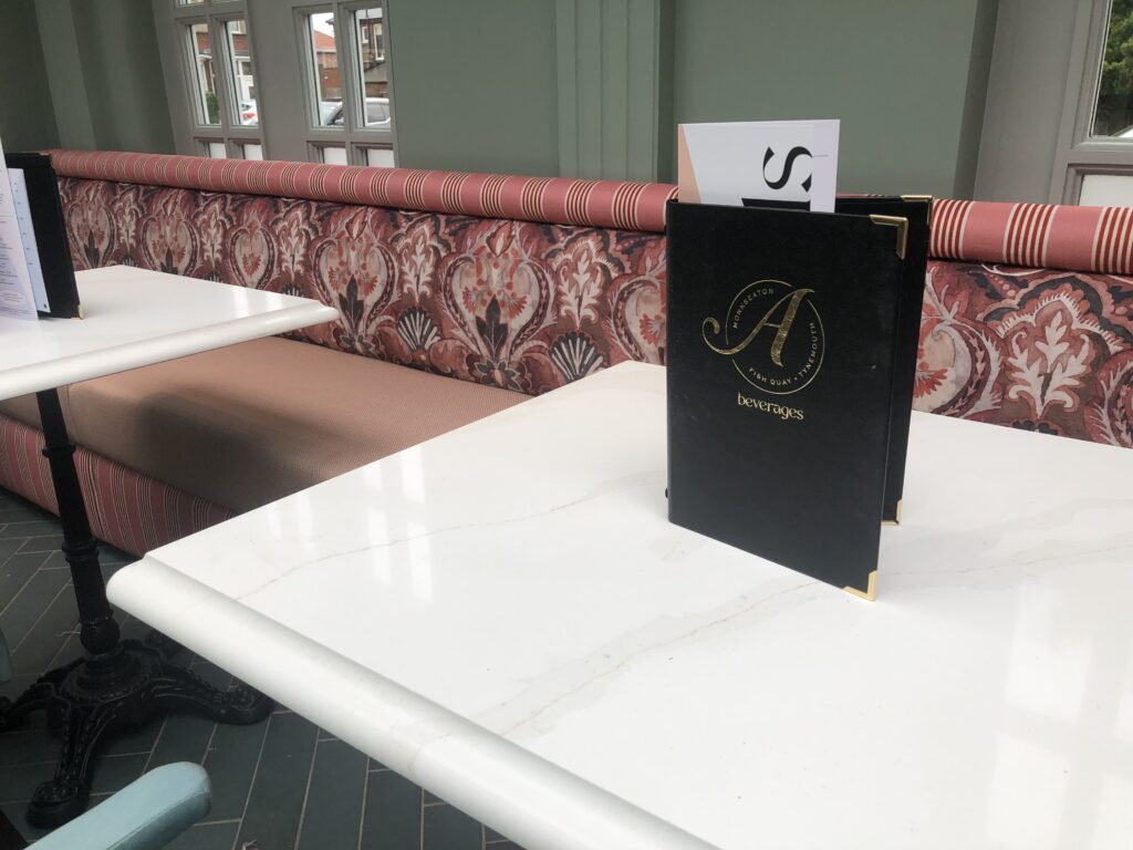 Close view of the pink patterned backrest and striped top roll beside an Allards menu.