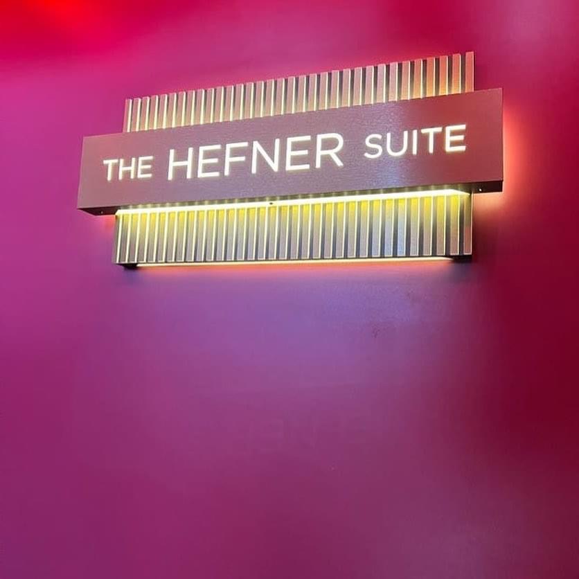Illuminated The Hefner Suite sign on a dark red wall.