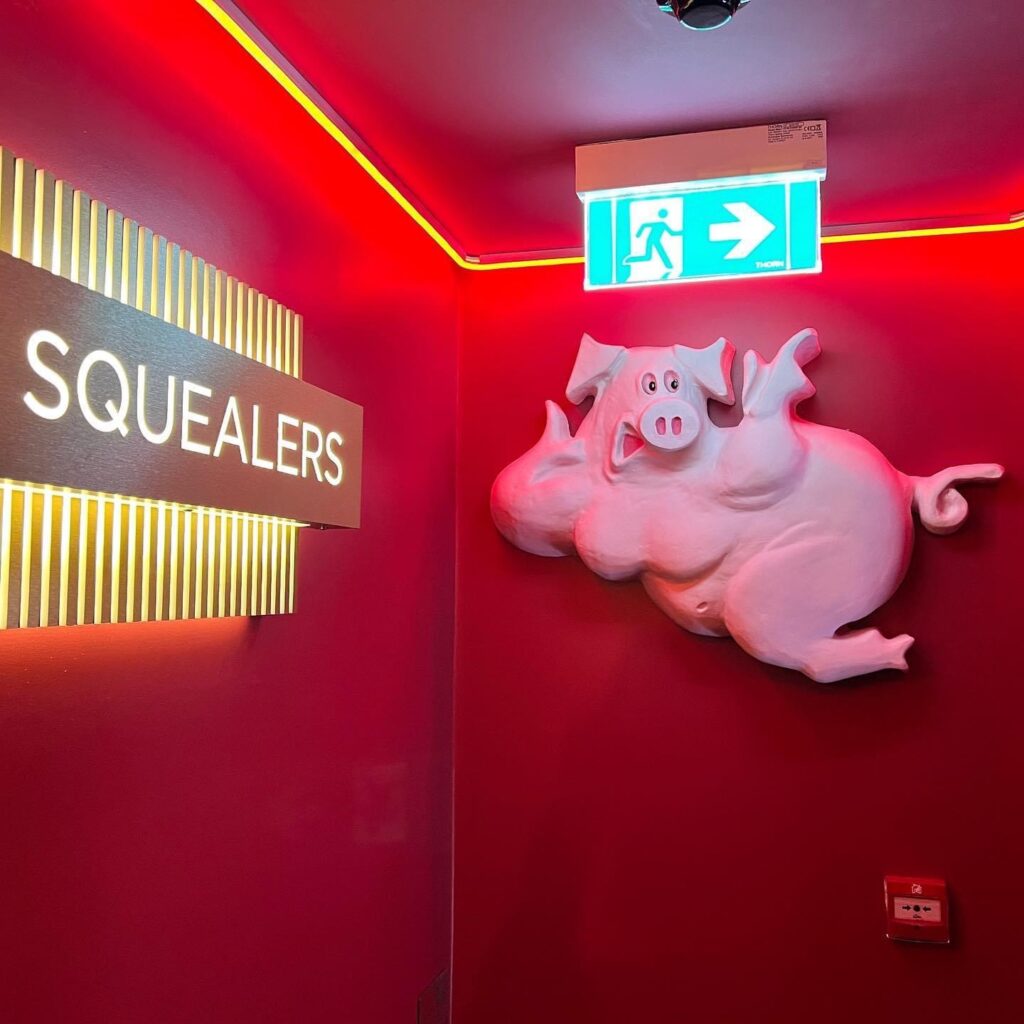 Squealers sign and a decorative pig figure in the red-painted corridor.