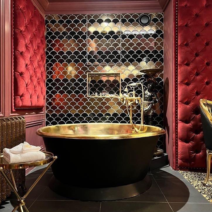 Gold-toned bath against mirrored fish-scale tiles and burgundy buttoned wall panels.