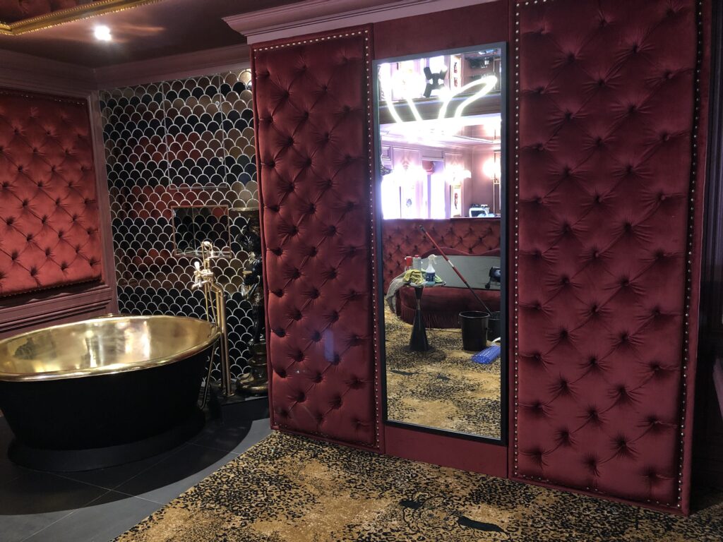 Deep burgundy buttoned wall panels on either side of a tall mirror, with closely spaced decorative studs.