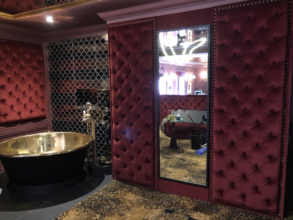 Angled view of a tall mirror between burgundy buttoned wall panels beside the bathing area.