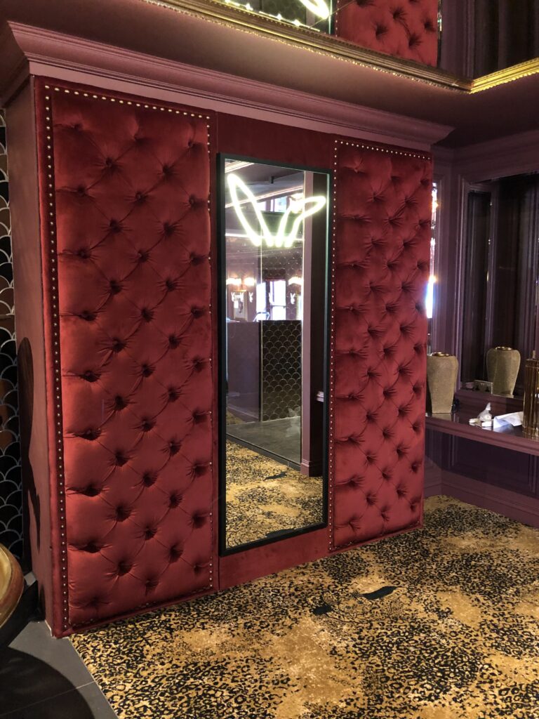 Close portrait view of buttoned burgundy upholstery and studded trim beside a tall rectangular mirror.