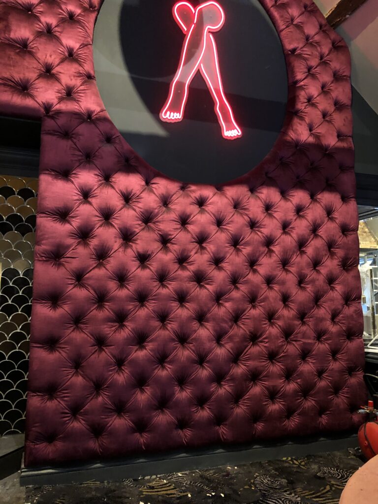 Burgundy upholstered feature wall surrounding a circular neon artwork, with diamond buttoning below.