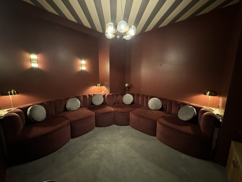 Rust-coloured wraparound seating with rounded pale scatter cushions beneath warm lights and a striped ceiling.