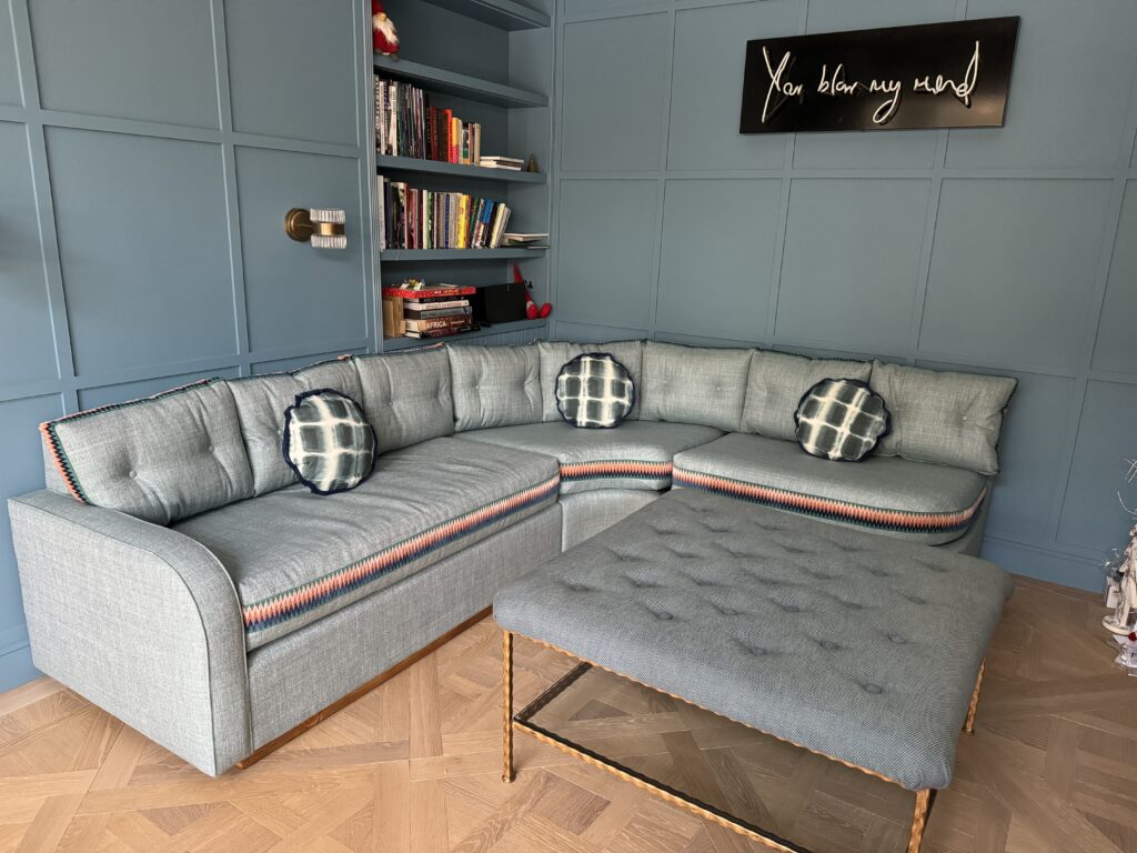 Blue-grey corner sofa with patterned cushion borders and round scatter cushions, beside a buttoned footstool.