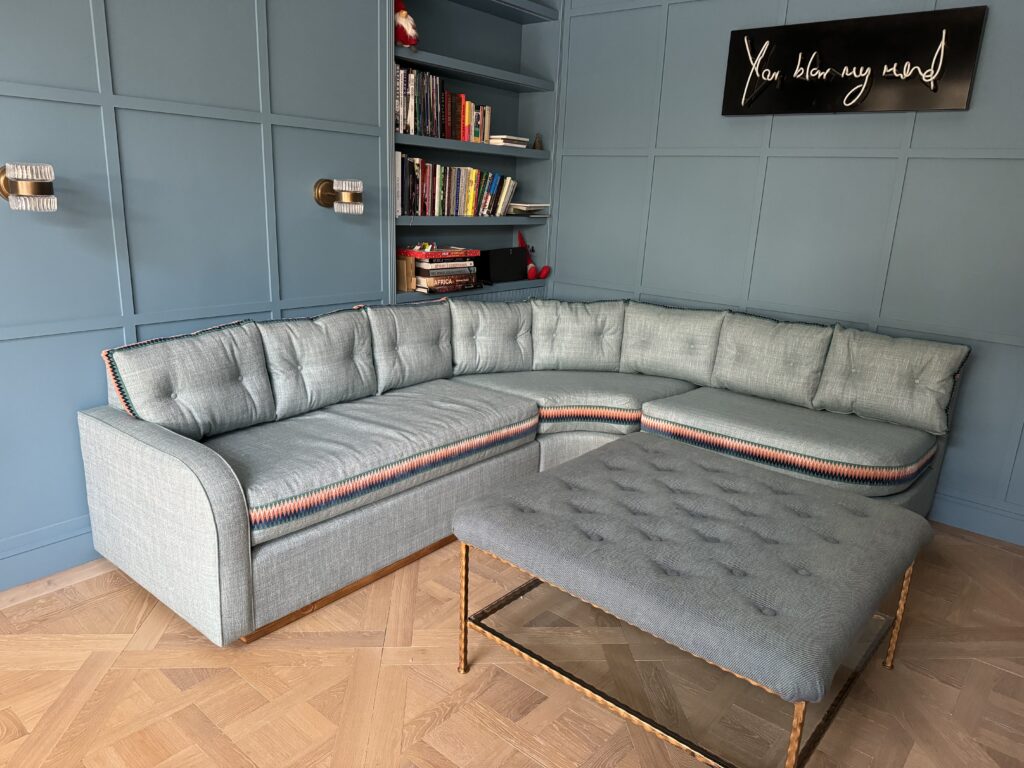 Closer view of blue-grey corner seating with peach and dark zigzag borders and a buttoned footstool on a slender metal frame.