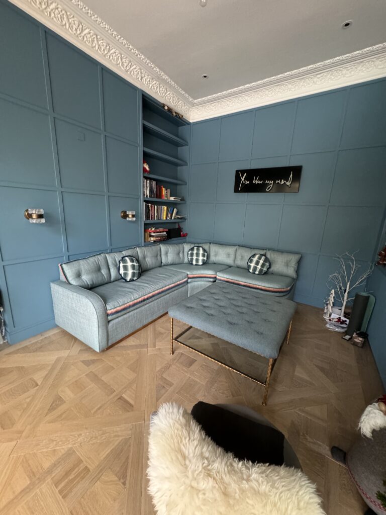 Blue-grey corner sofa styled with round patterned cushions, with a rectangular buttoned footstool in front.