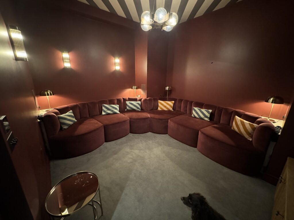 Wide view of rust-coloured wraparound seating with striped cushions and warm wall lights, with a dog in the foreground.