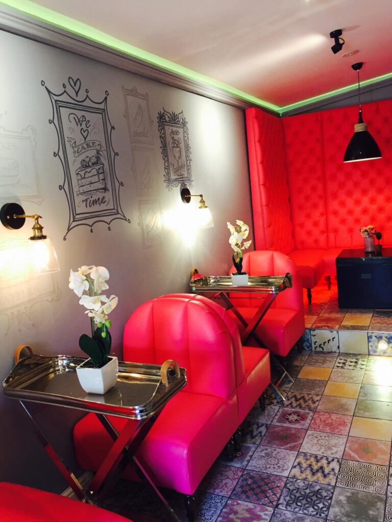 Vivid pink rounded chairs and a tall buttoned banquette beside illustrated walls and patterned tiles.