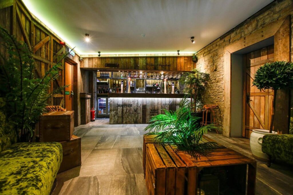 View from green seating towards a timber-fronted bar, with plants, stone walls and wooden tables.