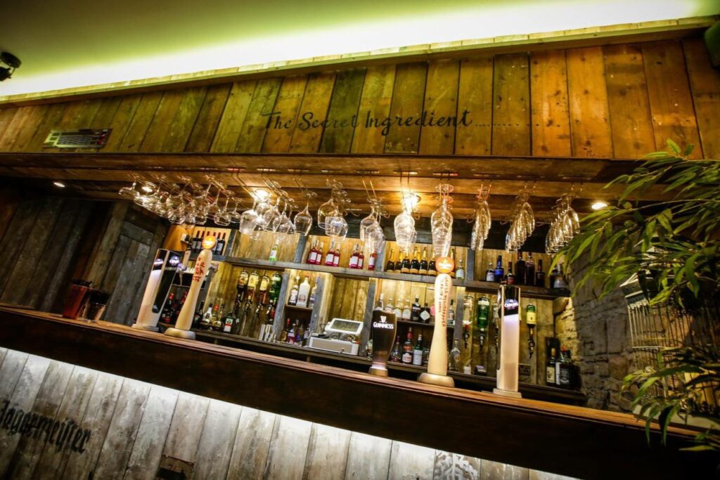 Close view of the timber bar, hanging glasses, bottles and the words The Secret Ingredient.