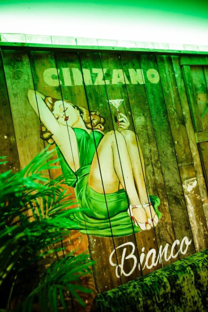 Cinzano Bianco illustration painted across timber boards above green upholstery.
