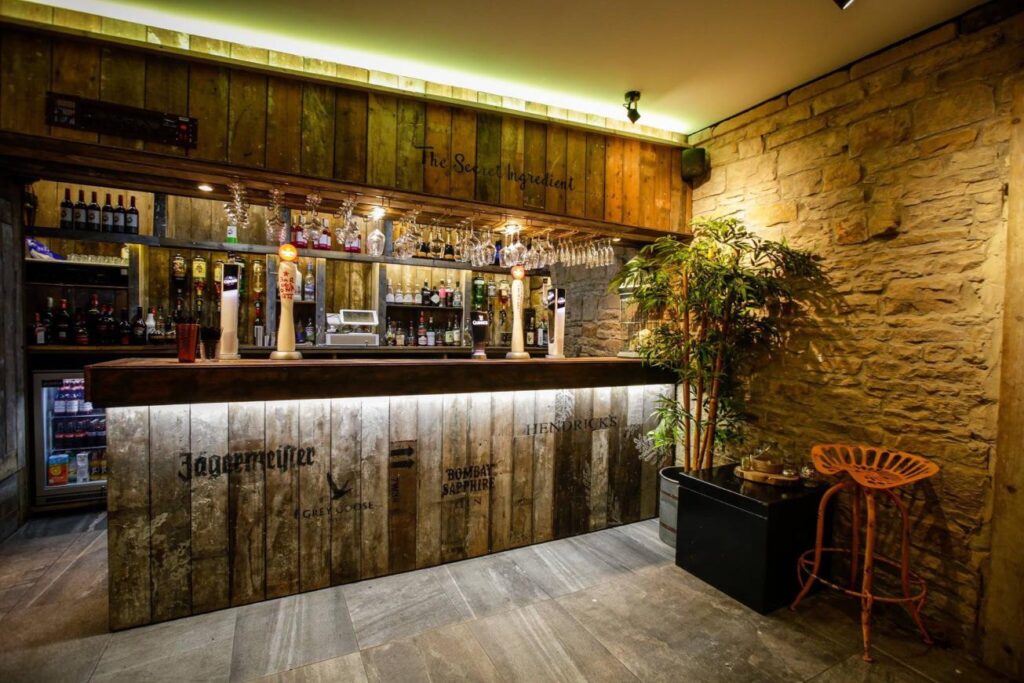 Timber-fronted bar beside exposed stonework, a potted tree and a metal stool.