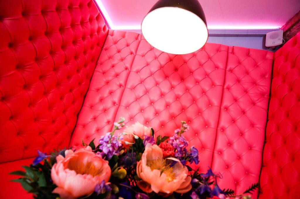 Close view of pink diamond-buttoned back panels behind flowers and a black pendant light.