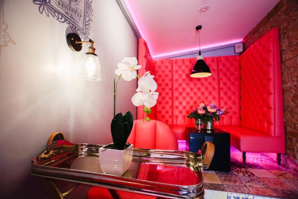 Metal tray table and white orchid in front of pink seating and a tall buttoned banquette.