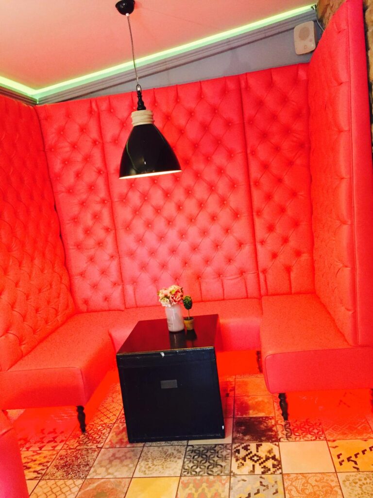 Tall pink buttoned upholstery wrapping around a three-sided seating alcove with a black table.