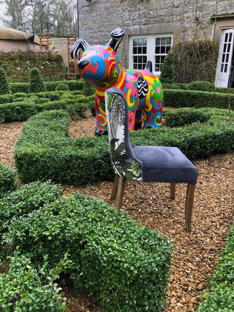 Upholstered chair with a blue-grey seat and botanical outer back, photographed beside a colourful dog sculpture.
