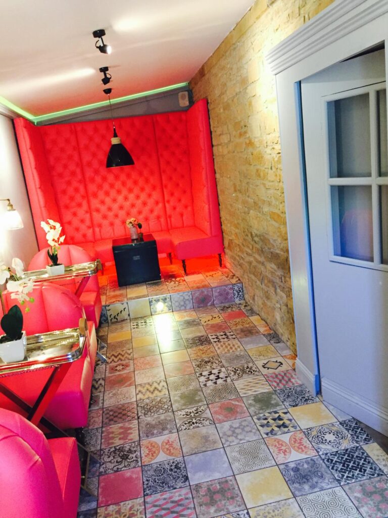 Long view of the pink seating area with patterned floor tiles, an exposed stone wall and a raised banquette.