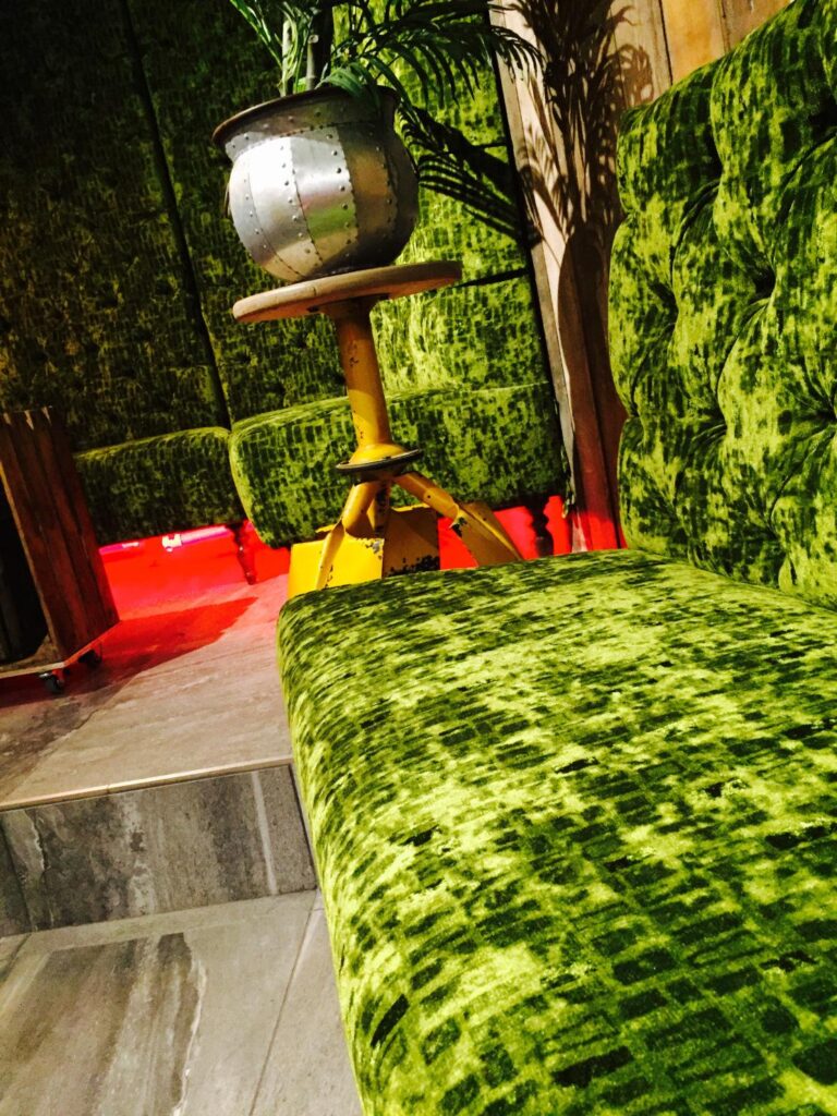Close view of textured green upholstery and buttoning, with a matching high-backed seat beyond.