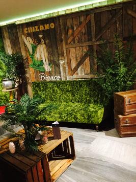 Compact view of green seating beneath a painted timber wall, with plants and crate tables.